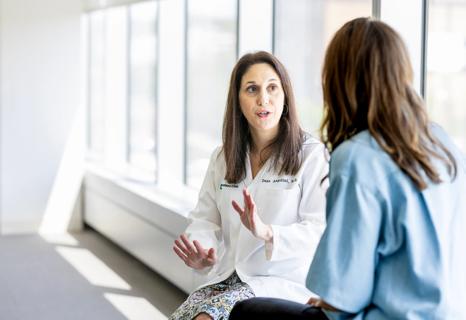 Physician having face-to-face conversation with patient near windows in white, bright room